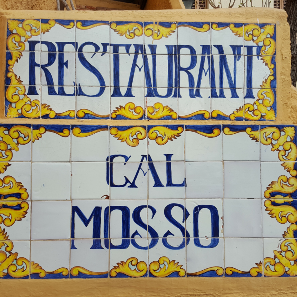 Primer plano del letrero de azulejos del restaurante Cal Mosso, con letras en azul y detalles decorativos amarillos.