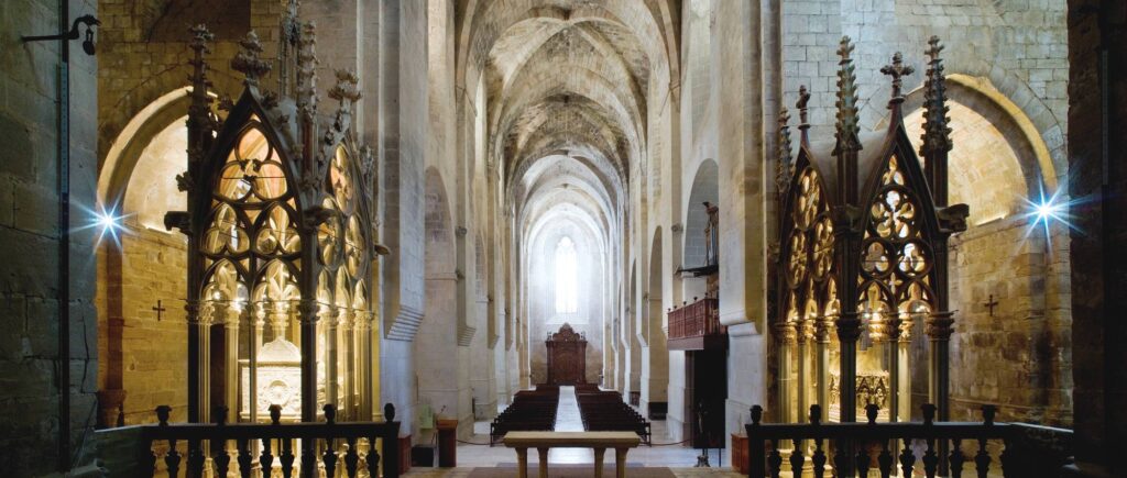 Interior de una iglesia gótica, con altas bóvedas de piedra, columnas y un altar iluminado al fondo.