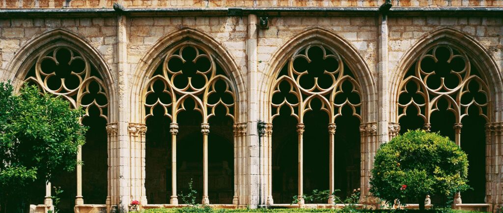 Arcos góticos de un claustro medieval rodeado de vegetación.